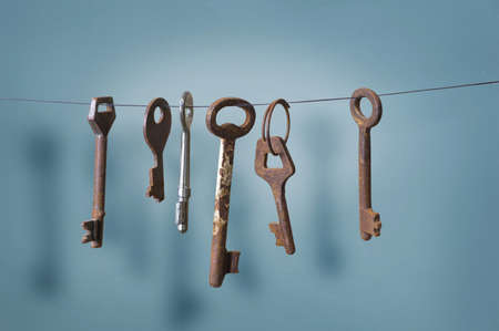 A different old retro rusty keys from different locks hanging on string with a drop shadow on a blue wallの写真素材