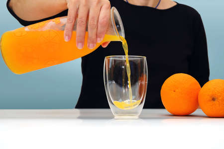 Female hand holding glass jar of fresh squeezed orange juice and pouring. selective focus
