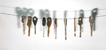 A different keys from different locks hanging on string with a drop shadow on a white wallの写真素材