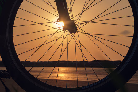 Close-up silhouette of a bike wheel at sunset. The sun shines through the wheel of a bicycle, selective focusの写真素材