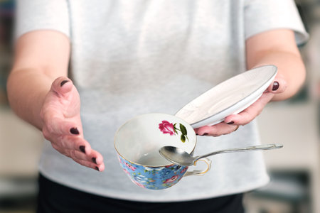 A female in a gray t-shirt dropping tea cup with and spoon, selective focusの写真素材