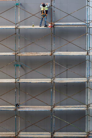 Construction worker on the scaffold prepares house facade wall for paintingの写真素材