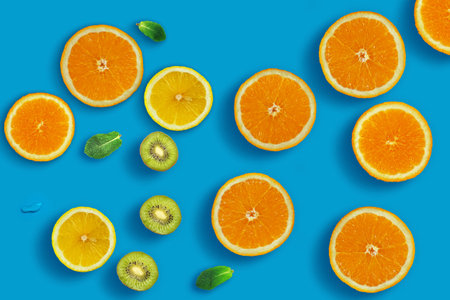 Fresh juicy slices of orange, kiwi fruit, lemon and mint leaves on bright blue background. Creative food background, top viewの写真素材