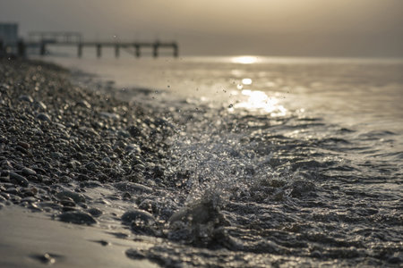 Small sea waves splashing at the beach with pebbles at sunset, selective focusの写真素材