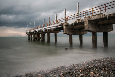 Frozen pier at the rocky beach gray sky backgroundの写真素材
