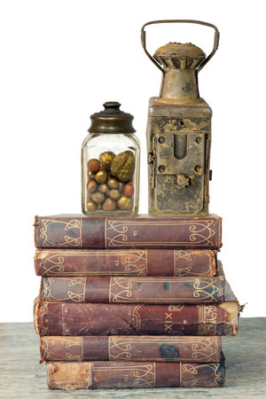 Vintage jar with nuts and old rusty lamp on a stack of old books, isolated on a white backgroundの写真素材