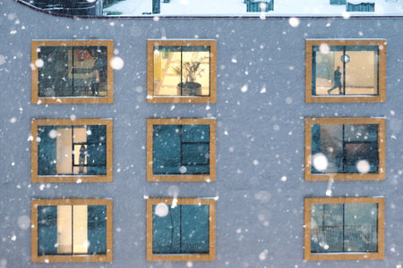 Illuminated windows of a building facade during snowfallの写真素材