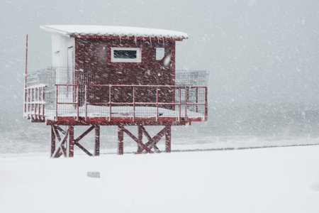 Red lifeguard tower construction on the coast during heavy snowingの写真素材