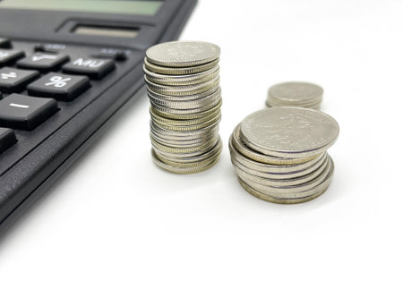 A stack of coins with a calculator on an isolated white background. Money, business.の写真素材