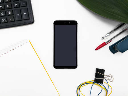 a notepad and a phone with a blank screen on a white table around stationery. Layout for the presentation.の写真素材