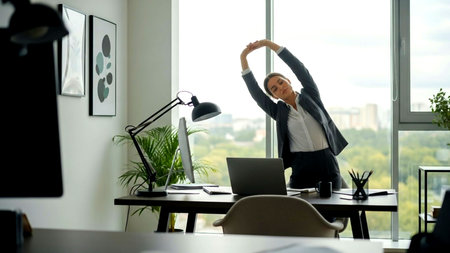 Professional woman in a contemporary office takes a refreshing stretch break, promoting well-being and active work-life balance for enhanced productivity and stress relief.の素材