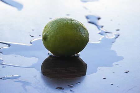 One green fresh lime on a wet clear blue surface with it's reflection.の写真素材