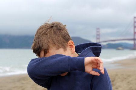 Portrait of a 10-year-old blond boy on the sandy beach of San Francisco on a cloudy day. The boy covered his face with his hand.の写真素材