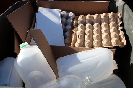 Mixed recyclables including plastic jugs, clear bottles, egg cartons, and cardboard in a recycling bin, promoting eco-friendly waste managementの写真素材