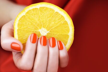 Female hand with bright red color manicure holding Orange sliceの写真素材