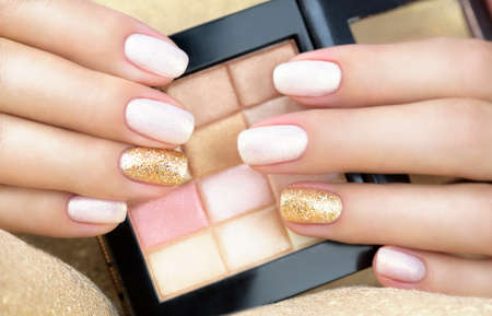 Female hands with golden manicure holding eyeshadow palette