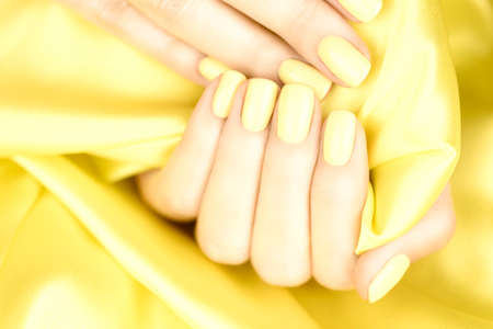 Female hands with yellow manicure on a yellow silk background.の写真素材