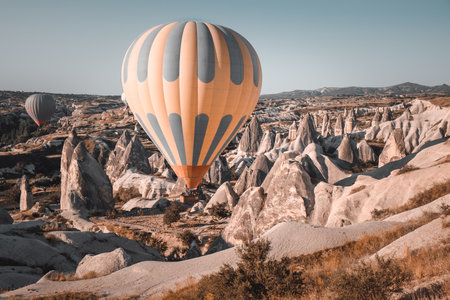 Colorful hot air balloon preparing to rise up for sunset watching tour over spectacular Cappadocia mountains. Wide landscape of Goreme valley. Vintage retro orange blue toning filter. Tourism, travelの写真素材