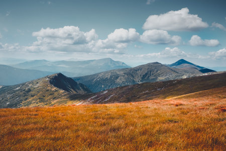 Majestic mountains colorful autumn landscape. Mountain peak, orange grass meadow and clouds in blue sky. Beautiful nature scenery. Majestic colorful natural background. Vintage tone filterの写真素材