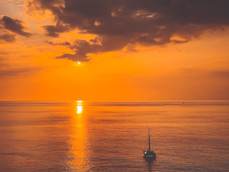 Bright orange sunset sky over sea and yacht boat. Dramatic cloudy sky, golden hour. Beautiful romantic scenic image of stunning seascape. Nature background. Summer vacation, travel, adventure conceptの写真素材