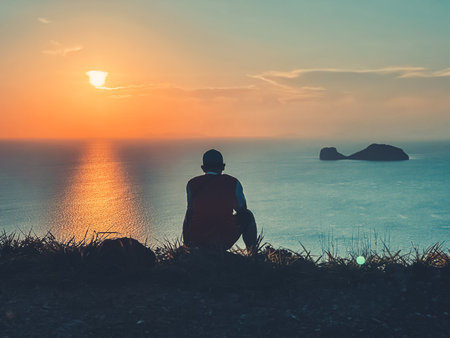 Man watching colorful tropical sunset. Back view silhouette against sea water and orange sky with sun and clouds. Amazing natural summer scenery. Travel, tourism, holiday, relax in Thailand islandの写真素材