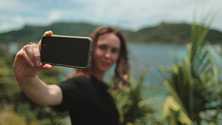 Woman makes selfie mobile photo enjoying tropical jungles and mountain lake landscape. Nature freedom adventure, happy vacation video call, girl tourist outdoors. Travel, tourism, holiday in Polynesiaの写真素材