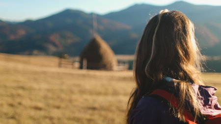 Tourist woman enjoy autumn sunset landscape in Carpathian mountains, Ukraine. Long hair caucasian girl looking on yellow grass field, village countryside. Travel, hiking, freedom and active lifestyleの写真素材
