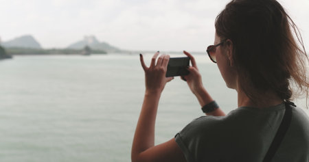 Woman making photo panorama of sea landscape on mobile phone. Back view tourist girl enjoy seascape while sailing ferry to Koh Phangan island in Thailand. Travel, tourism, holidayの写真素材