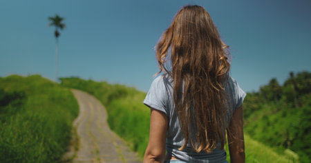 Tourist woman walking Campuhan Ridge Walk - tourist place to visit in Ubud, Bali island. Green field, blue sky. Outdoor lifestyle travel on summer holiday vacation. Close up back viewの写真素材