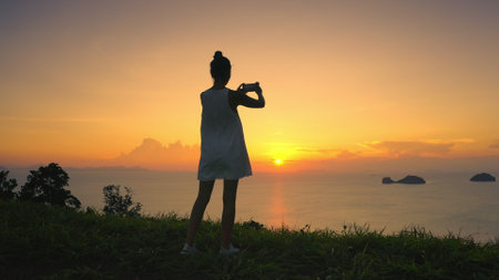 Person enjoy beautiful nature sunset landscape. Woman silhouette make photo bright orange sky and sea water coastline. Outdoor lifestyle travel on summer holiday vacation. Impressive colorful seascapeの写真素材