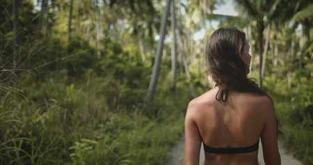 Girl walking in paradise fairy tale forest. Tropical green leaf palm trees. Caucasian woman trekking forest trail, lifestyle travel on summer holiday vacation. Asia, Thailand. Back viewの写真素材