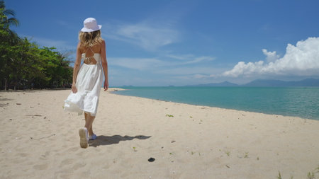 Woman in white dress walking wild tropic sand beach. Outdoor lifestyle travel on summer holiday vacation. Caucasian female relax, enjoy wild island nature. Bright sunny day, blue sky. Back viewの写真素材