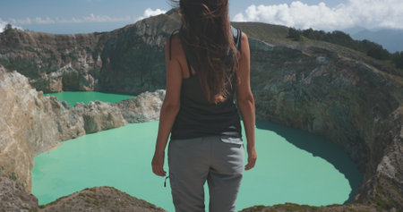 Tourist woman rises hands over volcanic Kelimutu blue crater lakes. Nature background. Travel destination. Beautiful wild landscape. Exotic summer vacation, hiking, relax.の写真素材