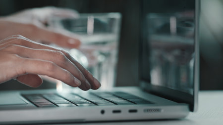 Female hands typing on computer. Business woman professional user worker typing on laptop notebook keyboard. Drink water from glass. Online work with pc software apps technologies, close up side viewの写真素材