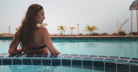 Panoramic shot woman relax in swimming pool. Long hair brunette back view enjoy her summer vacation...