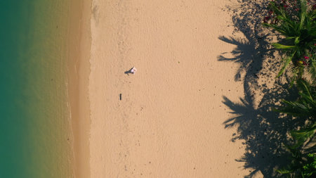 Tropical island travel background, people relax, enjoy summer holiday vacation. Woman in white dress and hat walking perfect empty sand beach with palm trees aerial top down view. Beach wallpaperの写真素材