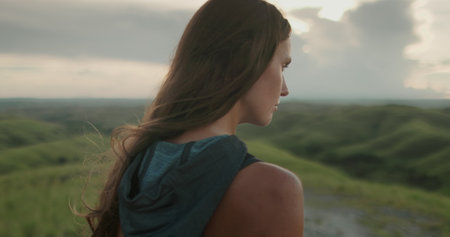 Woman relax green hills landscape at sunset. Long hair brunette girl looking on beautiful nature scene, close up side view. Freedom, happiness lifestyle. Travel, tourism, holiday. Slow motion 4Kの写真素材