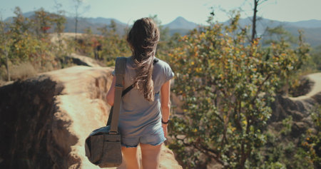 A woman wearing a backpack is trekking up a hill in Thailand.