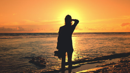 Girl stand on sandy beach, sun setting in background. Sky in warm colors, reflecting on calm ocean waves. Relax enjoy wild nature beauty on tropical island. Travel, tourism, holiday, active lifestyleの写真素材