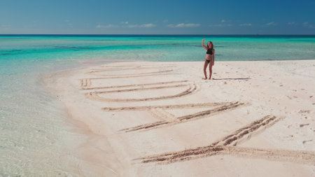 Woman enjoy perfect sand beach on tropical island in French Polynesia. Summer holiday concept. Happy beautiful girl wave hands. Exotic wild tropical island in turquoise sea. HOLIDAY written on sandの写真素材