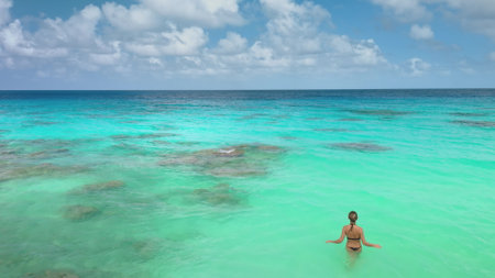 Young woman is enjoying a sunny day, walking into the turquoise lagoon water of rangiroa, a famous travel destination in french polynesiaの写真素材