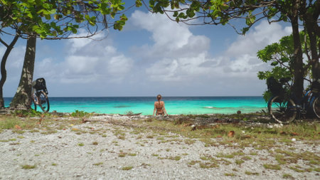 Young woman is taking a break from her bike ride, enjoying the view of the turquoise lagoon on a sunny day in rangiroa, french polynesiaの写真素材