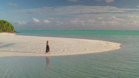 Young woman strolling on a tranquil beach, basking in the warm sun on untouched white sand of a tropical island with turquoise ocean and clear blue skyの写真素材