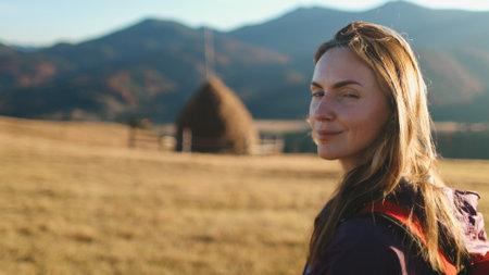 Tourist woman enjoy autumn sunset landscape in Carpathian mountains, Ukraine. Long hair caucasian girl looking on yellow grass field, village countryside. Travel, hiking, freedom and active lifestyleの写真素材