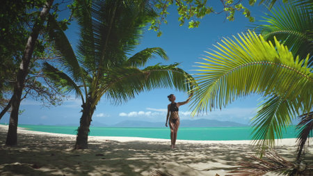 Slim girl in bikini walking sand tropical beach in Thailand, palm trees and clear blue sky. White sand beach and ocean in background. Female relax outdoor lifestyle travel on summer holiday vacation.の写真素材