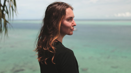 A woman stands in front of a body of water, appearing contemplative and connected to the natural environment.の写真素材