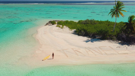 Aerial view of a woman walking on a tropical beach with travel written in the sand, enjoying a sunny...