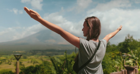 Young female tourist is embracing the beauty of a tropical landscape with the majestic mount mayon volcano in the background. She is enjoying her travel adventure in the philippinesの写真素材