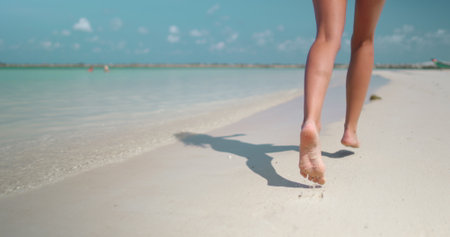 Woman legs barefoot running white sand beach tropical island pov. Slim female feet jogging, leisurely strolling along sea water waves. Relax, travel, summer holiday vacation. Slow back viewの写真素材