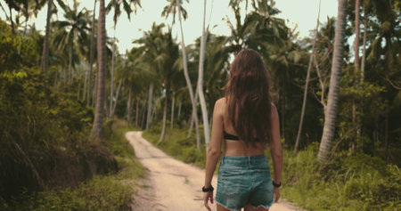 Female tourist walk jungle tropical forest trail. Long hair caucasian slim girl back view enjoy palm trees landscape. Exotic travel, tourism, holiday, hiking, active lifestyle. Nature summer landscapeの写真素材